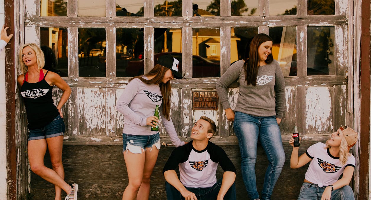 Five friends in Glory Dayz apparel relaxing against a weathered garage door