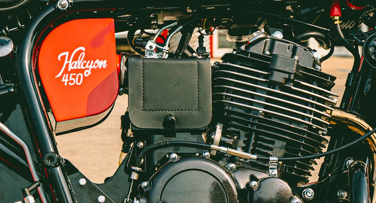 Close-up of a Janus Halcyon 450 motorcycle engine beside its red fuel tank