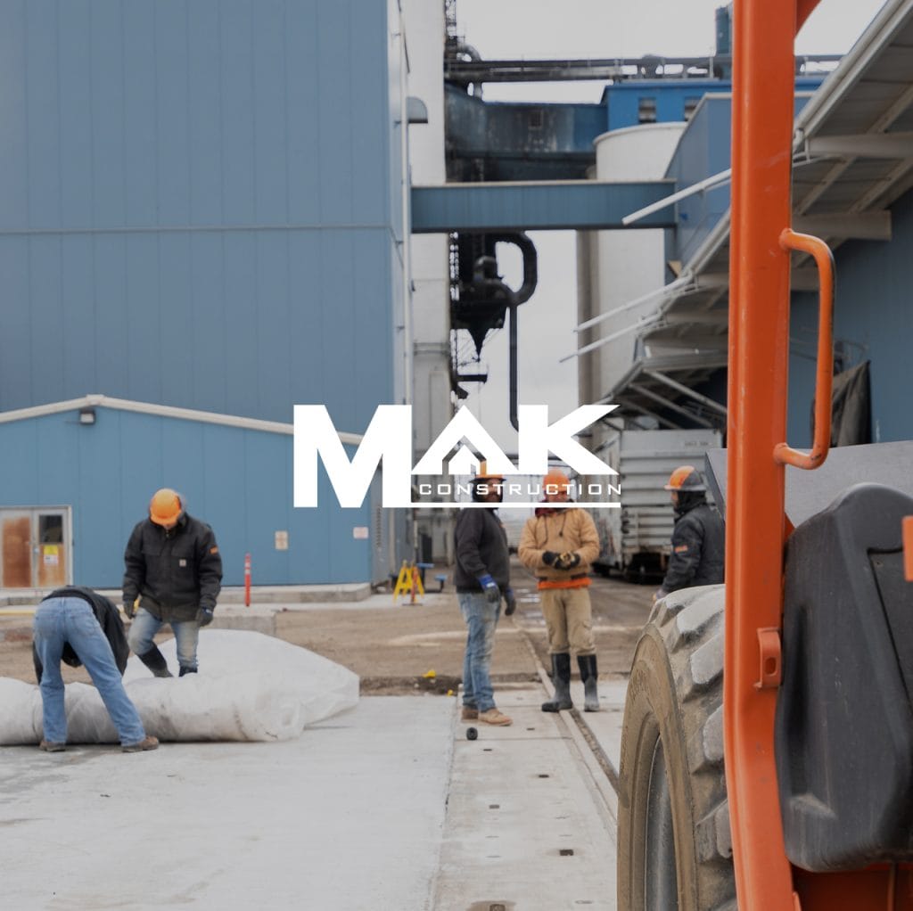 MAK Construction logo over a crew working beside a telehandler at an industrial site