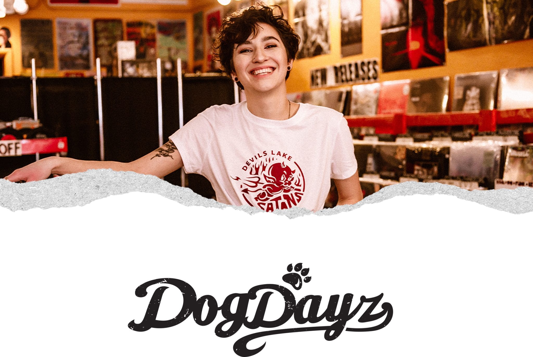 Person smiling in a Devils Lake Satans DogDayz T-shirt inside a record store, with the DogDayz logo below