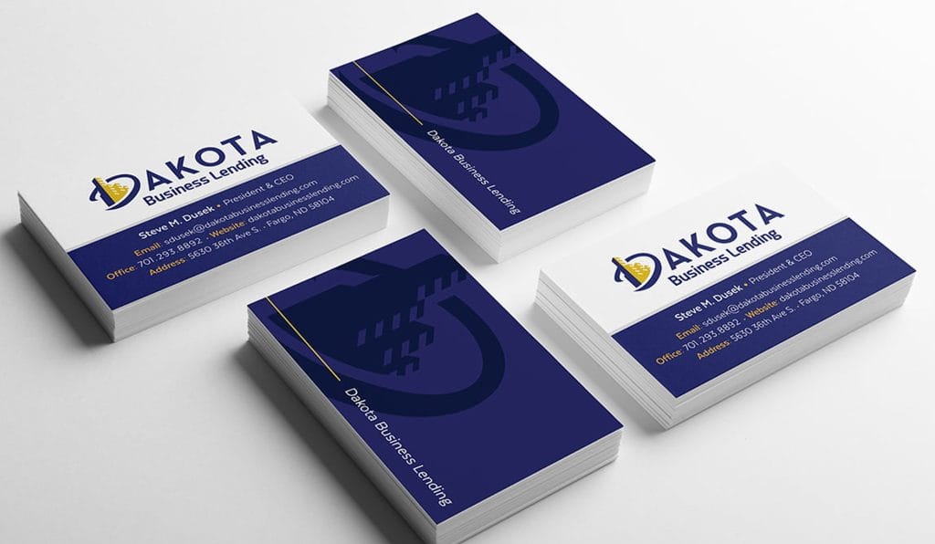 Stacks of Dakota Business Lending business cards in navy, white and gold
