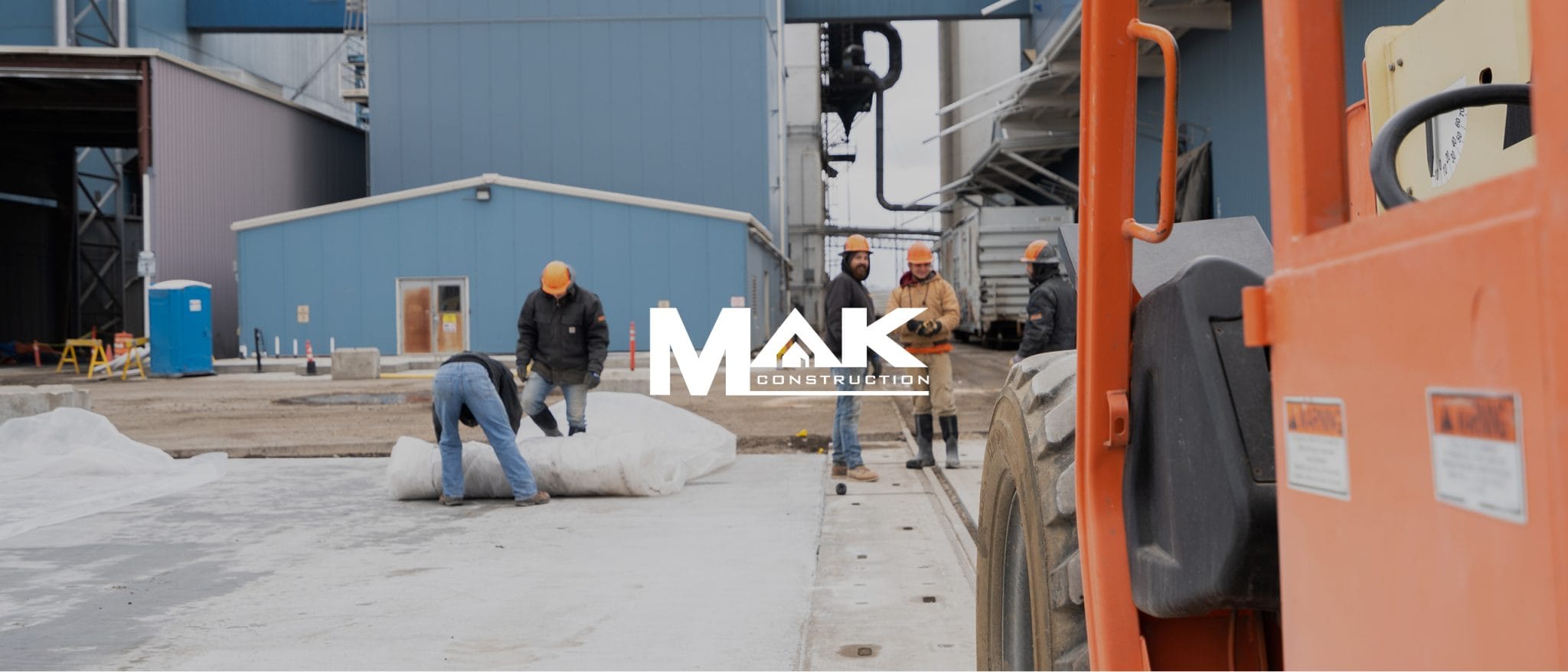 MAK Construction banner over a crew working beside a telehandler at an industrial site
