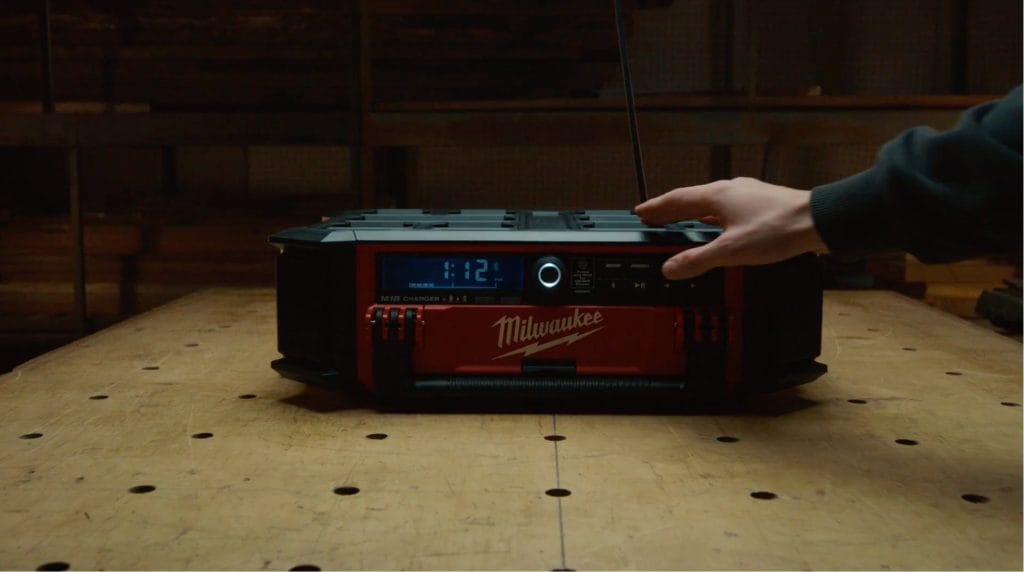 Video still of a hand switching on a Milwaukee jobsite radio resting on a workbench