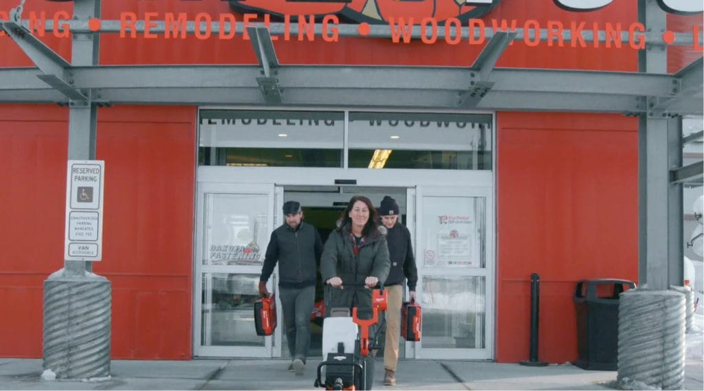 Video still of tradespeople leaving a supply store carrying Milwaukee power tools