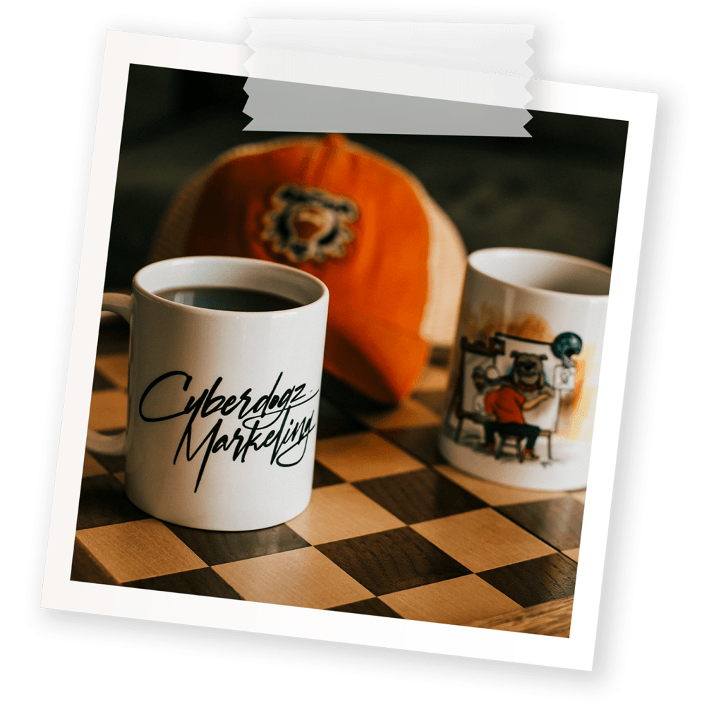Taped snapshot of a Cyberdogz Marketing coffee mug beside an orange branded cap on a checkered table